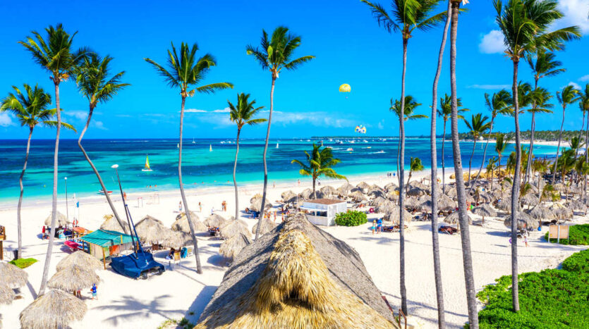 Couple walking along Punta Cana beach at sunset with golden skies, swaying palm trees, and gentle ocean waves