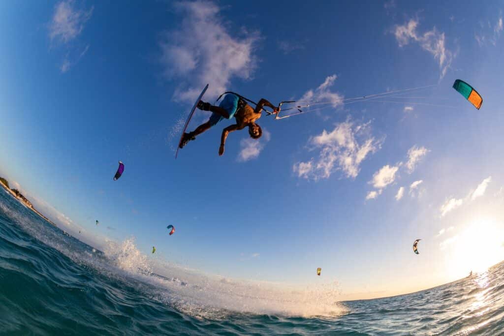 Kiteboarder catching air above turquoise waves in Cabarete, with palm trees and sandy beach in the distance.