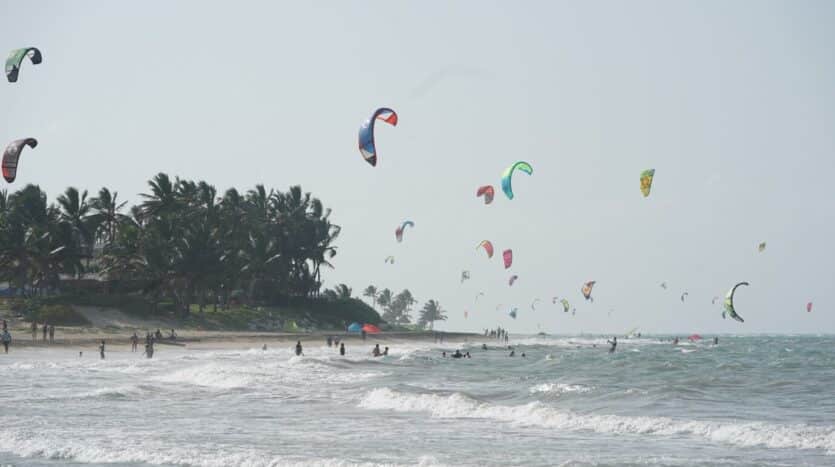 Person kiteboarding over clear blue waters in Cabarete, Dominican Republic, with a sunny sky and waves in the background