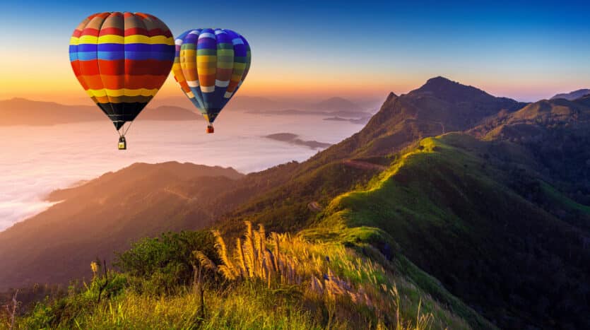 Colorful hot air balloon floating above green hills and farmland in the Dominican Republic countryside.