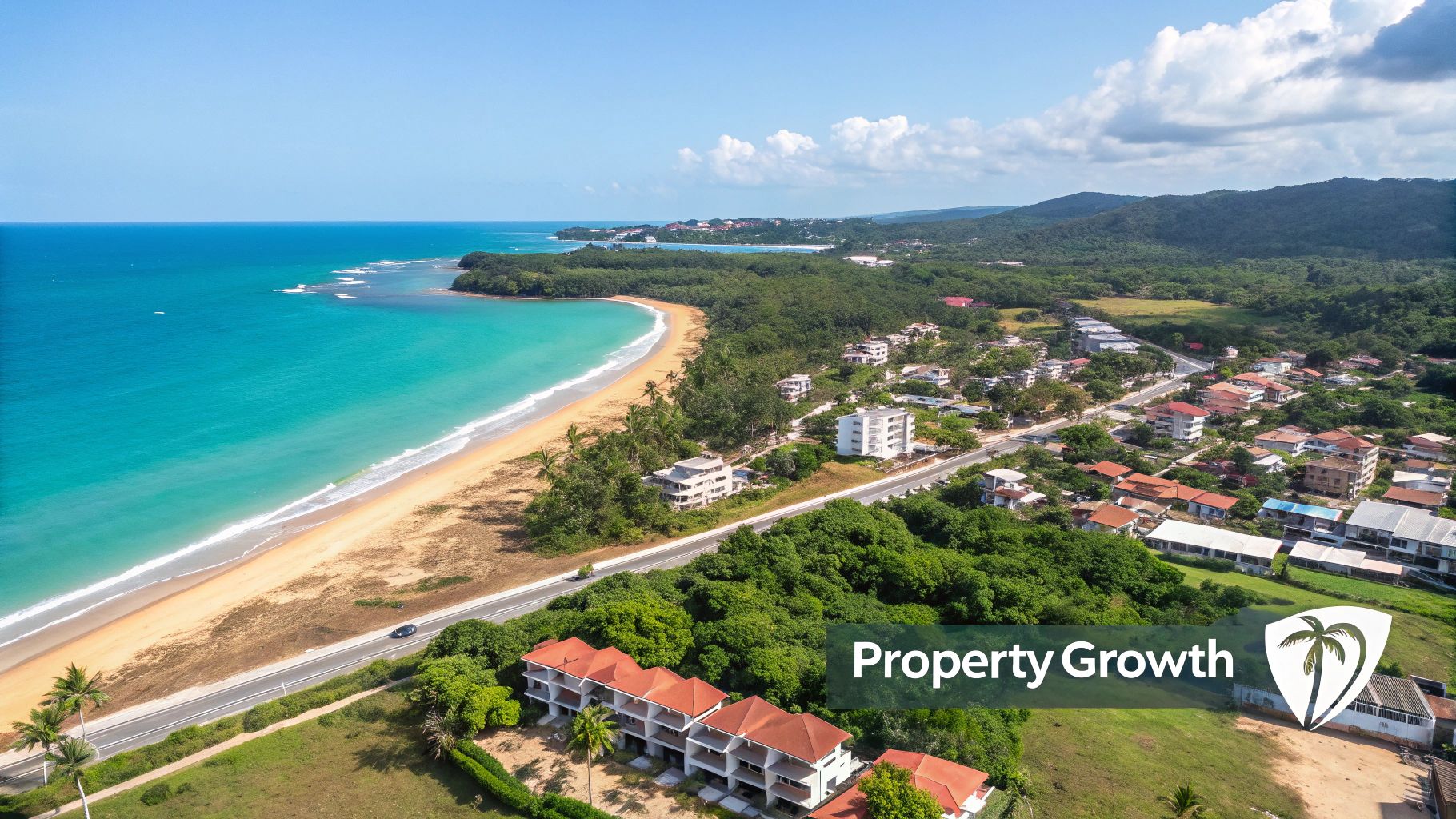 Aerial view of a vibrant coastal town with a sandy beach, turquoise ocean, and lush green hills.