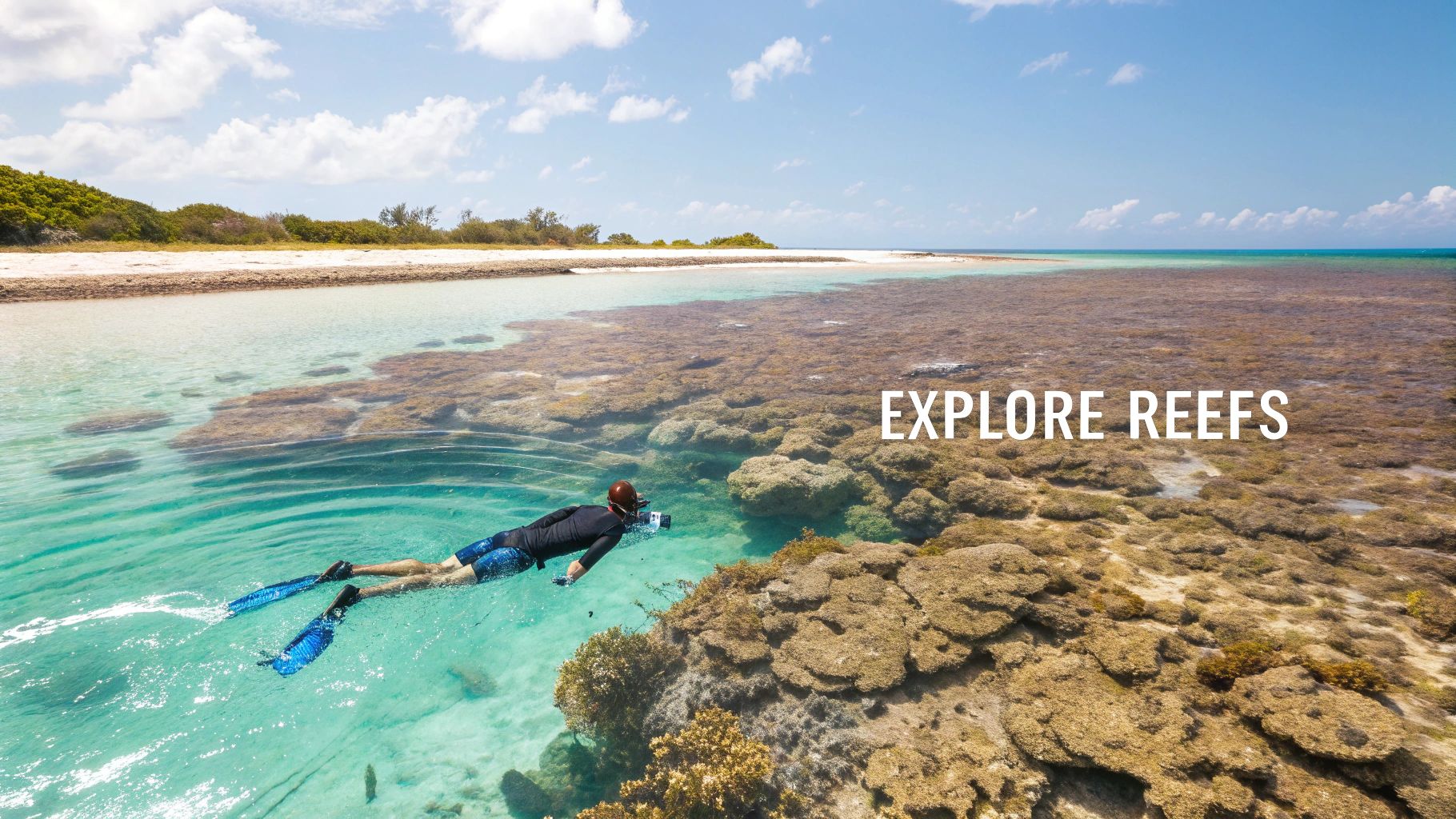 Snorkeler swimming above a beautiful coral reef in crystal clear water near a tropical island shore.